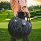 Women's golf handbag with textured golf-ball design, stylish round shape, and durable leather handles for sporty elegance.